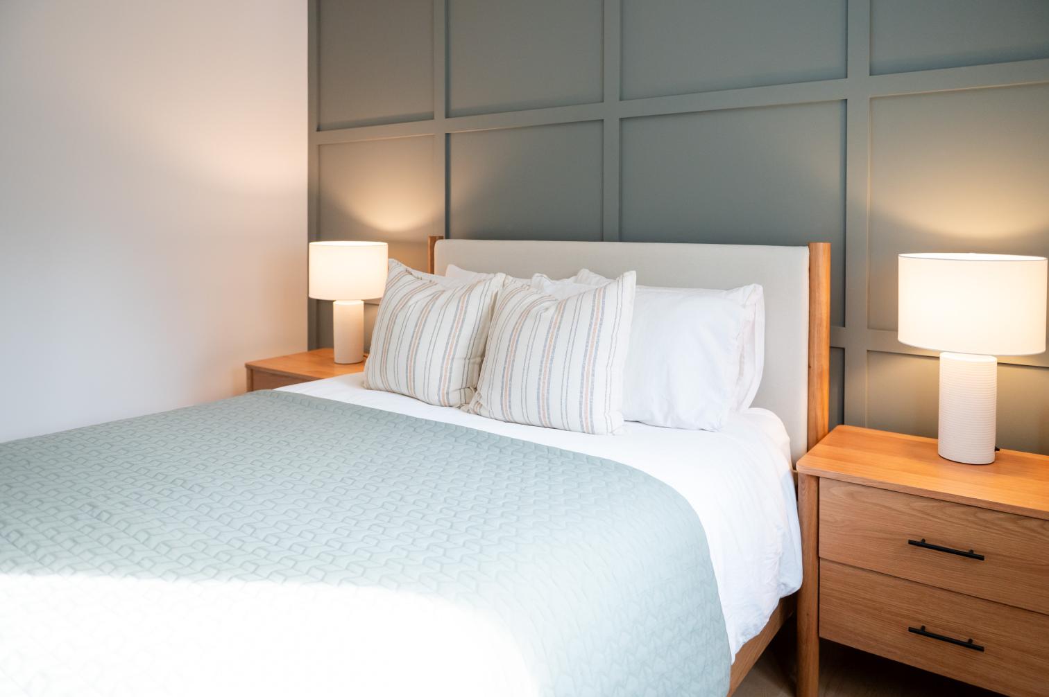 Elegant primary bedroom with sage feature wall, white oak nightstands and soft neutral bedding in Whitby, Ontario